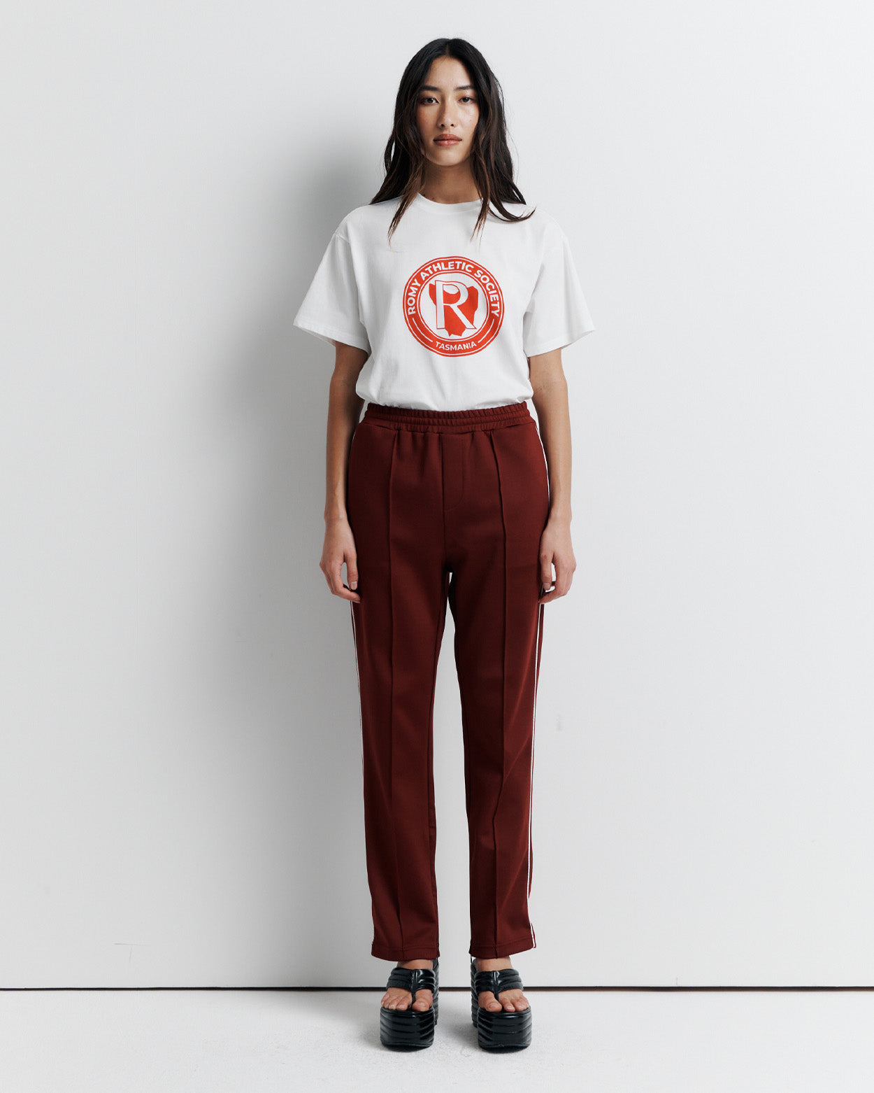 The RAS Track Pant features a comfortable elastic waistband, contrast piping, and pinstitch detailing. Designed with a straight leg, side pockets, internal drawstring, and invisible ankle zips. Finished with the signature Romy Athletic Society 'R' embroidery at the back.