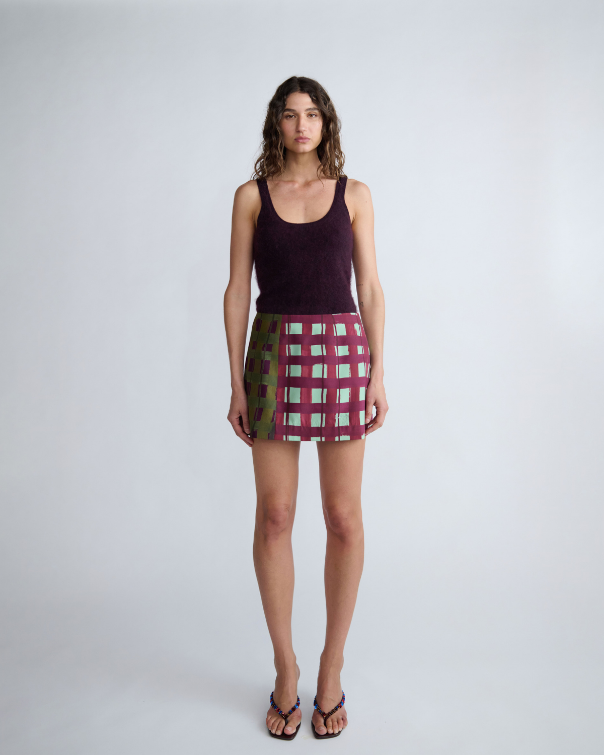 Model wearing the ROMY Ardent Skirt in burgundy and olive check, styled with a plum scoop neck knit tank.