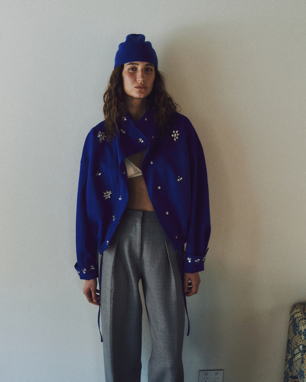 Editorial image of the ROMY Cropped Forever Jacket worn open with grey trousers and a matching blue beanie.