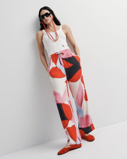 June Pant in pink, red and black abstract print, styled leaning pose on model.