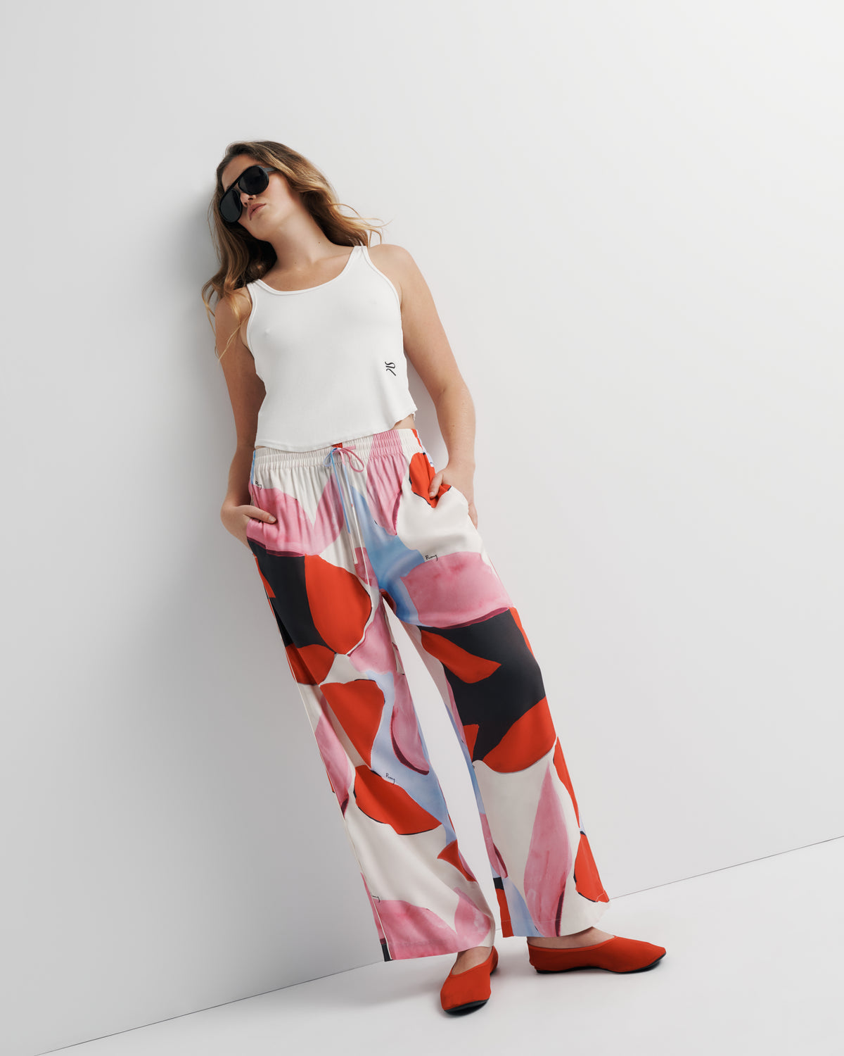 June Pant in pink, red and black abstract print, styled leaning pose on model, alternate.