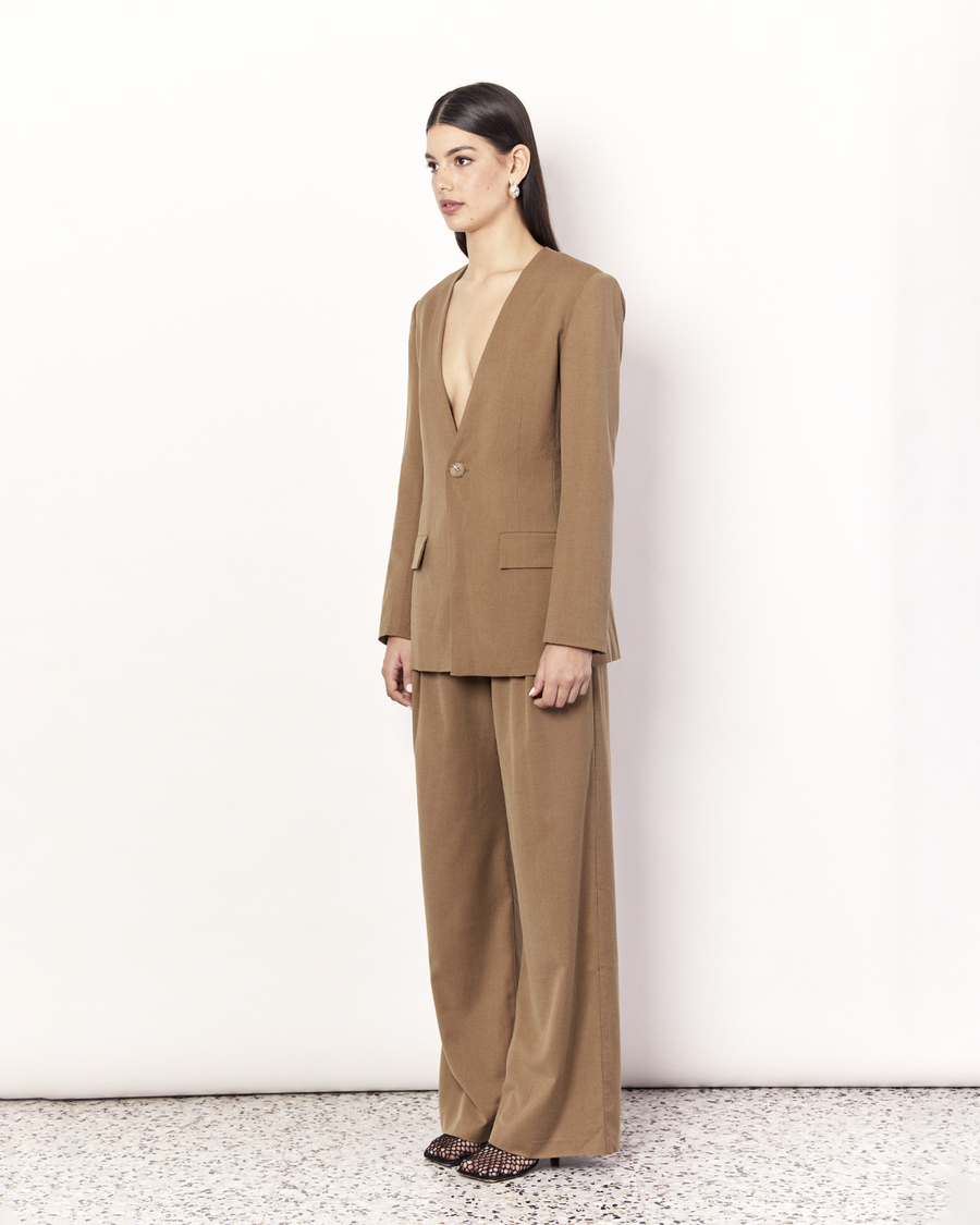 The Collarless Blazer is a versatile tailored silhouette featuring two front pockets, a button closure and a collarless neckline. It is fully lined and is crafted from a soft wool blend in Tan. Now available at Romy.