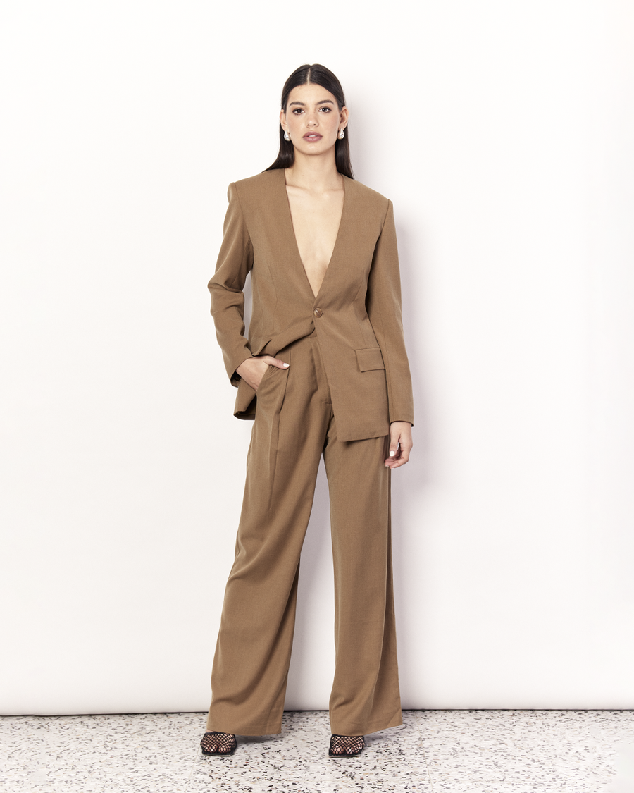 The Collarless Blazer is a versatile tailored silhouette featuring two front pockets, a button closure and a collarless neckline. It is fully lined and is crafted from a soft wool blend in Tan. Now available at Romy.