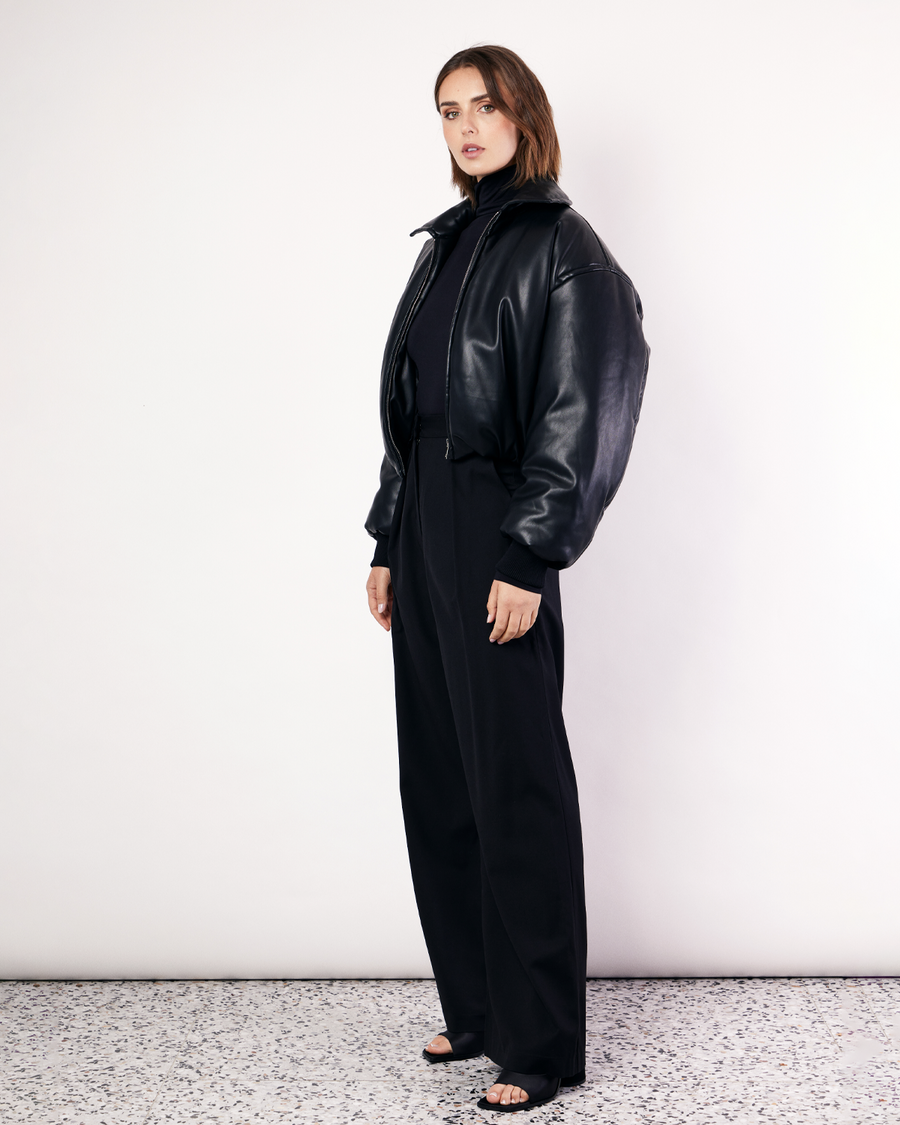 Our best-selling Padded Bomber Jacket is a must-have in your winter wardrobe, featuring a collar, gathered hem, and ribbed knit cuffs. It is crafted from a buttery soft Vegan Leather in Black. Now available at Romy. 