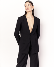 The Collarless Blazer is a versatile tailored silhouette featuring two front pockets, a button closure and a collarless neckline. It is fully lined and is crafted from a soft wool blend in Black. Now available at Romy. 