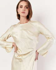 The Long Sleeve Wrap Dress boasts a fluid form and elevated style, featuring gathered detailing and a leg split. It is crafted from 100% Crushed Acetate in a Lemon hue. Now available at Romy. 