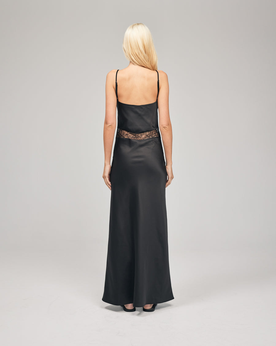 A black maxi dress features a delicate floral lace cut-out that accentuates the waist. It is bias-cut to effortlessly skim the body, creating a sleek and flattering silhouette. Show now.