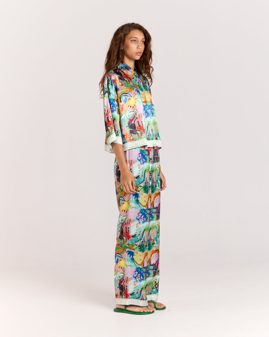 Discover the charm of our cropped oversized shirt, crafted from a matte twill blend of viscose and recycled rayon. Adorned with an eye-catching artist print by Jake Pedro and a contrasting Romy hem, this versatile piece can be worn open over a swimsuit, paired with a singlet, or styled with matching pants for a complete look.