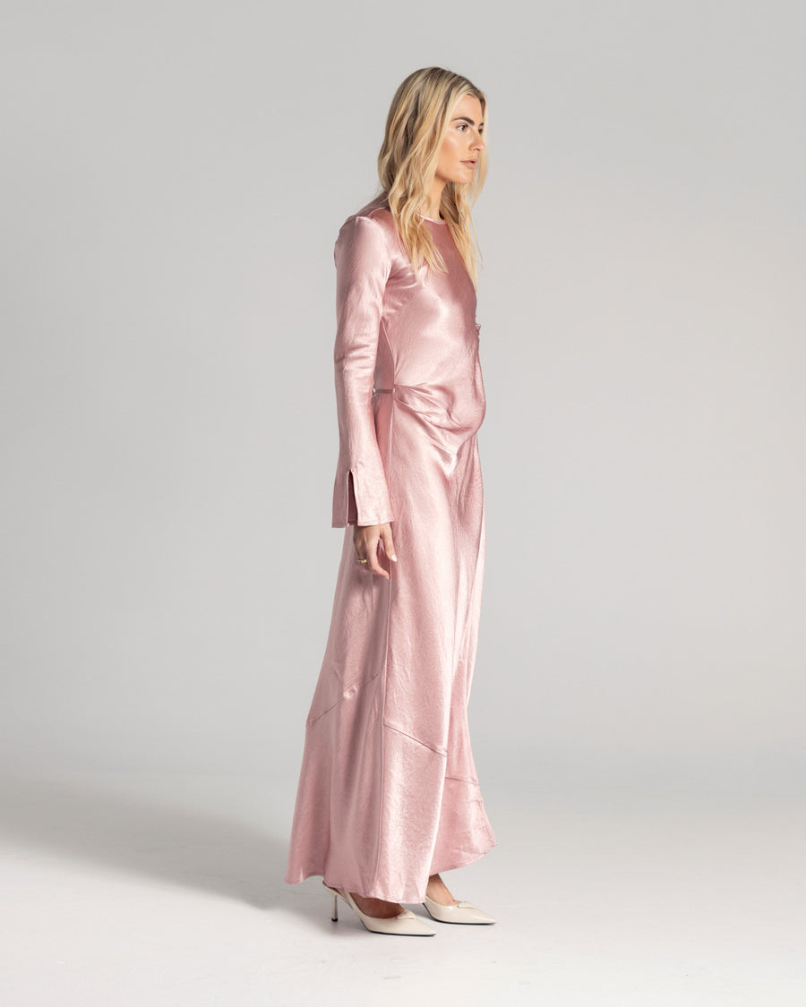 The Long Sleeve Wrap Dress boasts a fluid form and elevated style, featuring gathered detailing and a leg split. It is crafted from 100% Crushed Acetate in a Blush hue. Now available at Romy. 